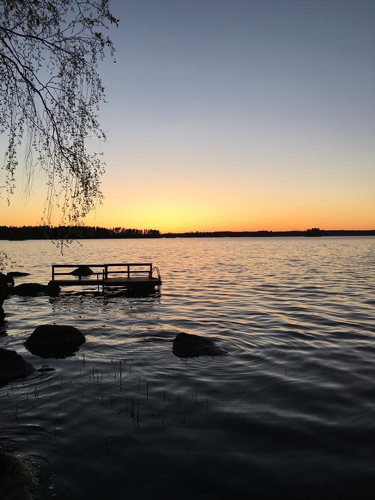 Juhannusyö mökkirannassa ja oranssi auringonlasku.
