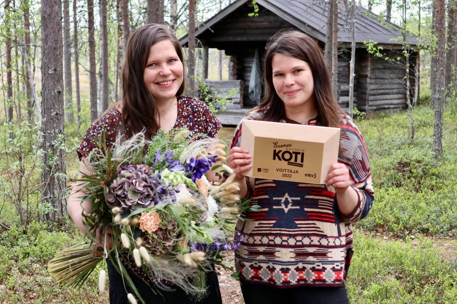 Voittajat Heidi ja Henna Jyrkkä poseeraavat mökkinsä edustalla.