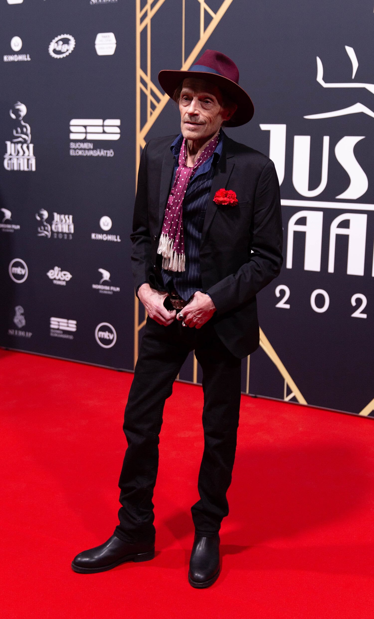 Ilkka Heiskanen oli yhdistänyt mustaan pukuunsa viininpunaisen hatun ja samaa sävyä olevan huivin.